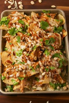 nachos with meat, cheese and cilantro in a pan on a wooden table