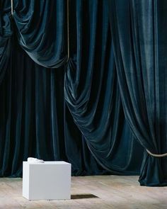 a white box sitting on top of a wooden floor next to blue curtained walls