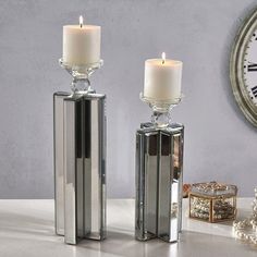 two glass candlesticks sitting next to each other on a table with a clock in the background