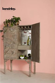 a cabinet with wine glasses and bottles on it in front of a wall painted pink