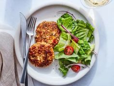 a white plate topped with meat patties next to a green salad and silverware