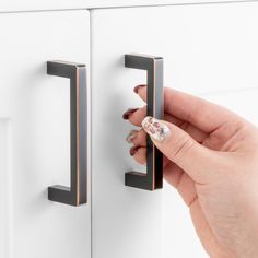 a woman's hand is holding onto the handles of a cabinet door with two knobs