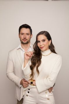 a man and woman standing next to each other in front of a white wall, posing for the camera