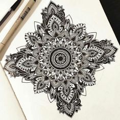 a drawing of a flower with black and white designs on paper next to two markers