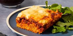 a piece of lasagna on a plate next to a green leafy salad