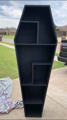 a black book shelf sitting on top of a sidewalk next to a car parked in front of a house