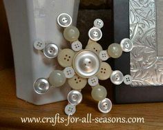 a white vase sitting on top of a wooden table next to a buttoned snowflake