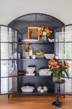 an open bookcase with flowers and plates on the top shelf in front of it