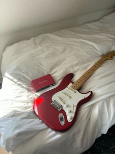 a red guitar sitting on top of a white bed