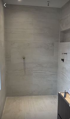 an empty bathroom with white tile walls and flooring is seen in this image from the shower area