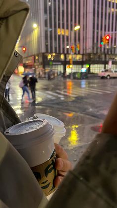 a person holding a cup of coffee in the rain on a city street at night