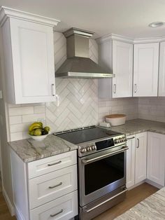 a kitchen with white cabinets and stainless steel stove top oven in the center, surrounded by marble counter tops