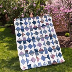 a woman is holding up a quilt on the grass