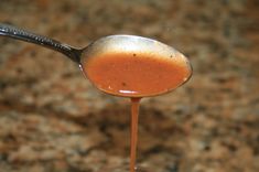 a spoon filled with sauce on top of a counter next to a brown and black surface