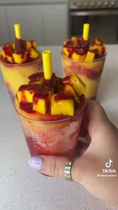 three glasses filled with fruit sitting on top of a white counter next to a person's hand