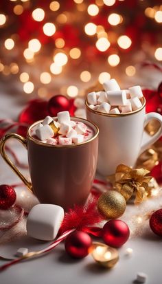 two mugs filled with hot chocolate and marshmallows next to christmas decorations