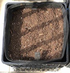 soil in a black plastic container sitting on top of a tile floor next to a planter