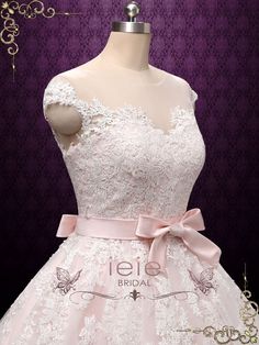 a white dress with pink ribbon on the waist and shoulder, is displayed in front of a mannequin