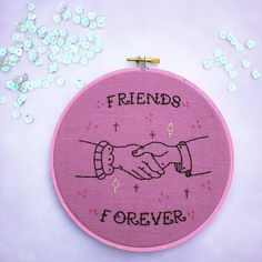 a pink embroidered wall hanging with two hands holding each other and the words friends forever written on it