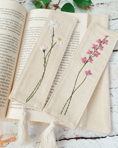 three bookmarks with flowers on them sitting next to an open book