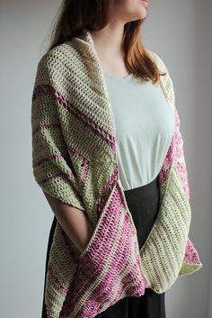 a woman wearing a knitted shawl standing in front of a window with her hands on her hips