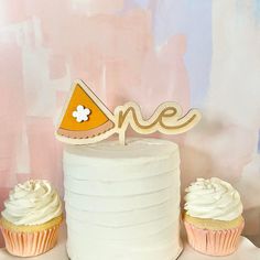 two cupcakes sitting on top of a white cake next to a one sign