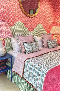 a bed with pink and green bedspread next to a blue night stand in front of a round mirror