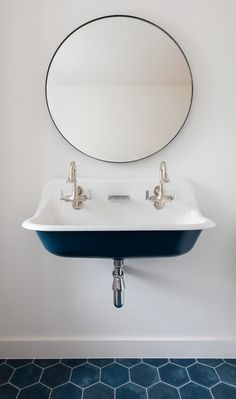 a white sink sitting under a round mirror in a bathroom next to a blue tiled floor