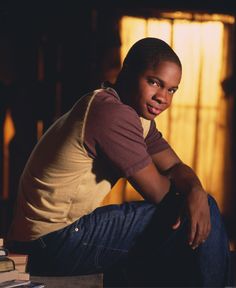 a young man sitting on top of a table next to a stack of books in front of a window