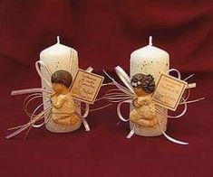 two candles with angel figurines on them sitting next to each other in front of a red background