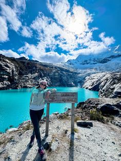 a woman standing on top of a mountain next to a blue lake with mountains in the background