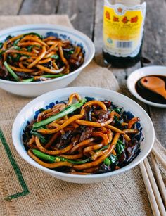 two white bowls filled with stir fry noodles and sauce on top of a wooden table