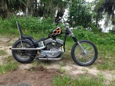 a motorcycle parked on the side of a dirt road next to grass and trees in the background