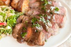 a white plate topped with meat and veggies next to a glass of wine