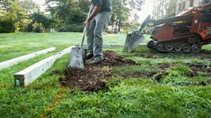 a man standing in the grass with a shovel and digging dirt on top of it