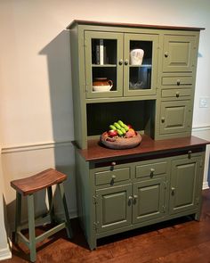 a green hutch with some fruit on top and two stools next to it