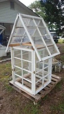 a small white greenhouse sitting on top of a pallet in front of a house