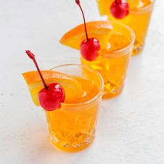 three glasses filled with orange juice and cherries