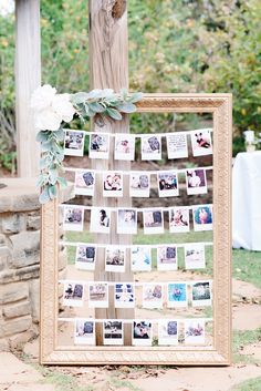 a wooden frame with photos hanging from it and flowers on the top is next to a tree