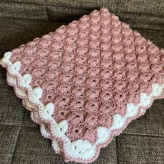 a pink and white crocheted blanket sitting on top of a couch