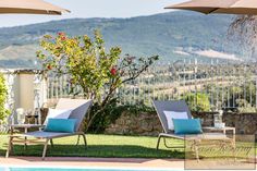 two lounge chairs sitting next to a swimming pool with an umbrella over it and mountains in the background