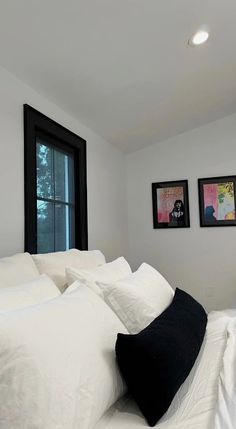 a bed with white sheets and pillows in a bedroom next to two pictures on the wall