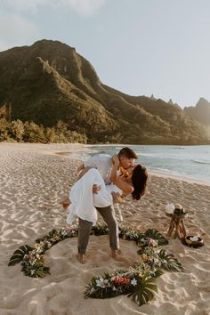 a bride and groom kissing on the beach in front of their wedding arch with flowers