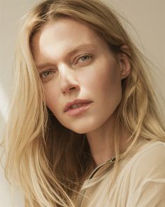 a woman with long blonde hair wearing a beige shirt and looking off to the side