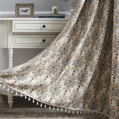 a bed with a white and brown flowered blanket on top of it next to a dresser