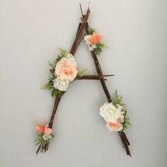 a flowered letter made out of sticks and twigs on a white wall with flowers