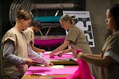 some women are doing crafts together at a table with pink sheets on it and one woman is cutting paper