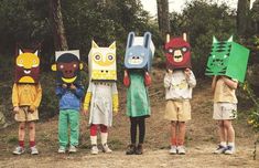 five children with paper masks on their heads standing in a line, all wearing different costumes