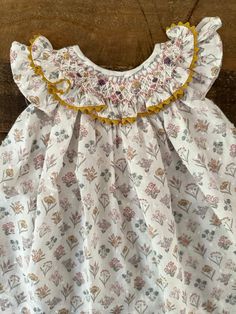 a white dress with yellow trim and floral print on the bottom, sitting on a wooden surface