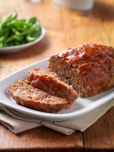 sliced meatloaf on a plate with green beans and salad in the back ground